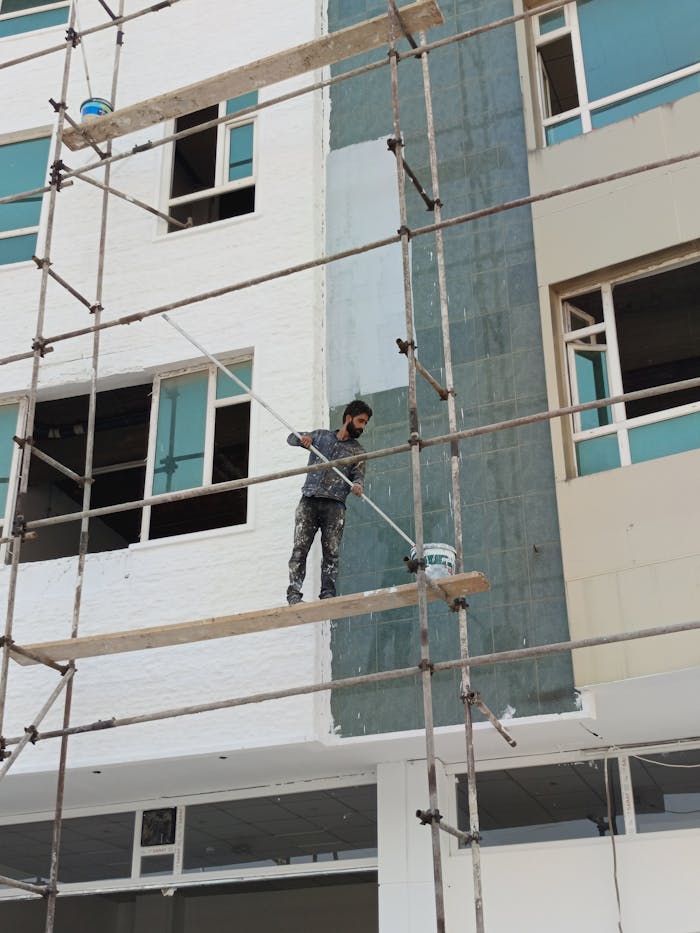 Construction worker on scaffolding painting a building exterior.