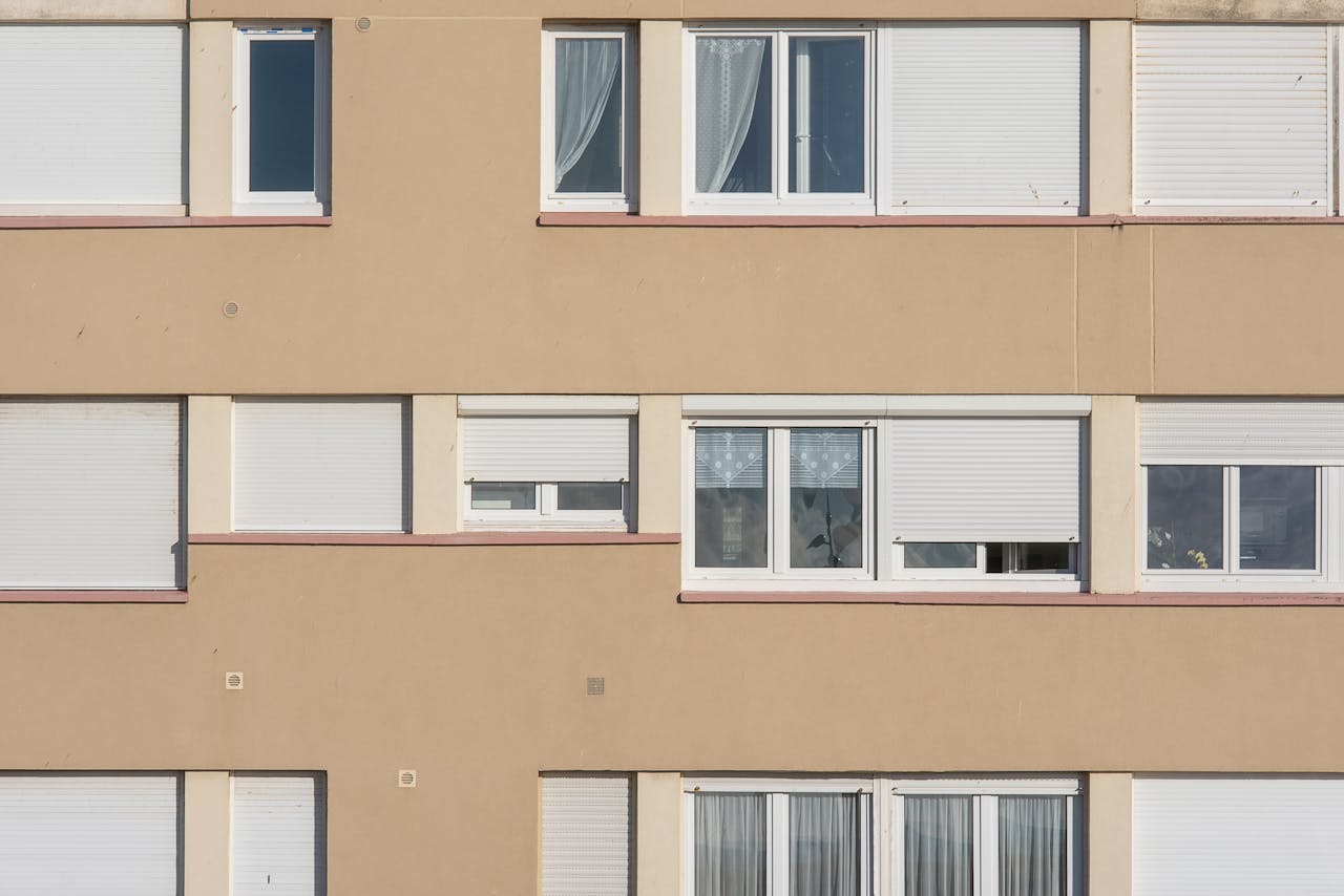 services-04 Symmetrical arrangement of windows on a beige urban building facade with closed shutters.