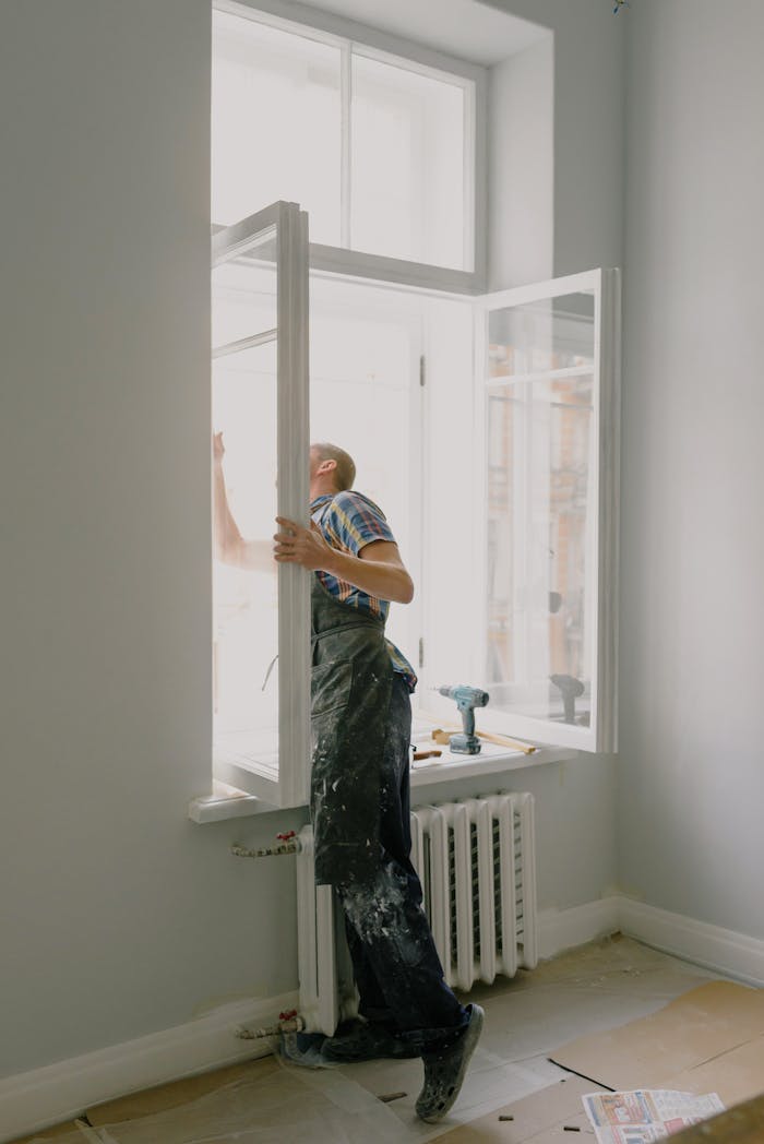 our-experience Side view of anonymous handyman in uniform mounting window frame during renovation process in flat