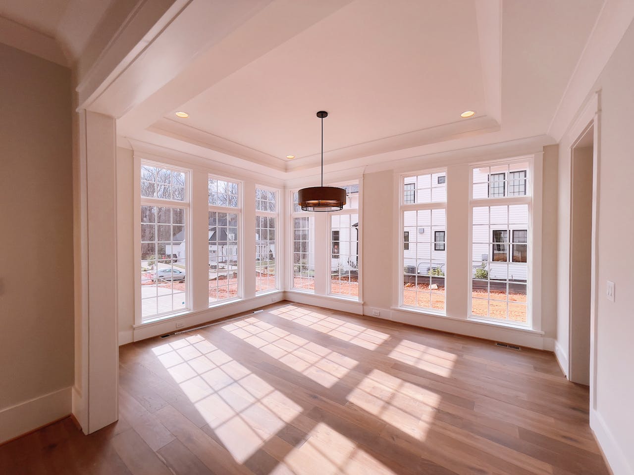 services-03 Spacious indoor room featuring large windows, hardwood floor, and modern pendant lamp.